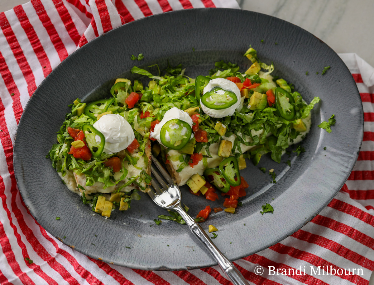 White Chicken Enchilada on plate covered in lettuce, tomato, sour cream