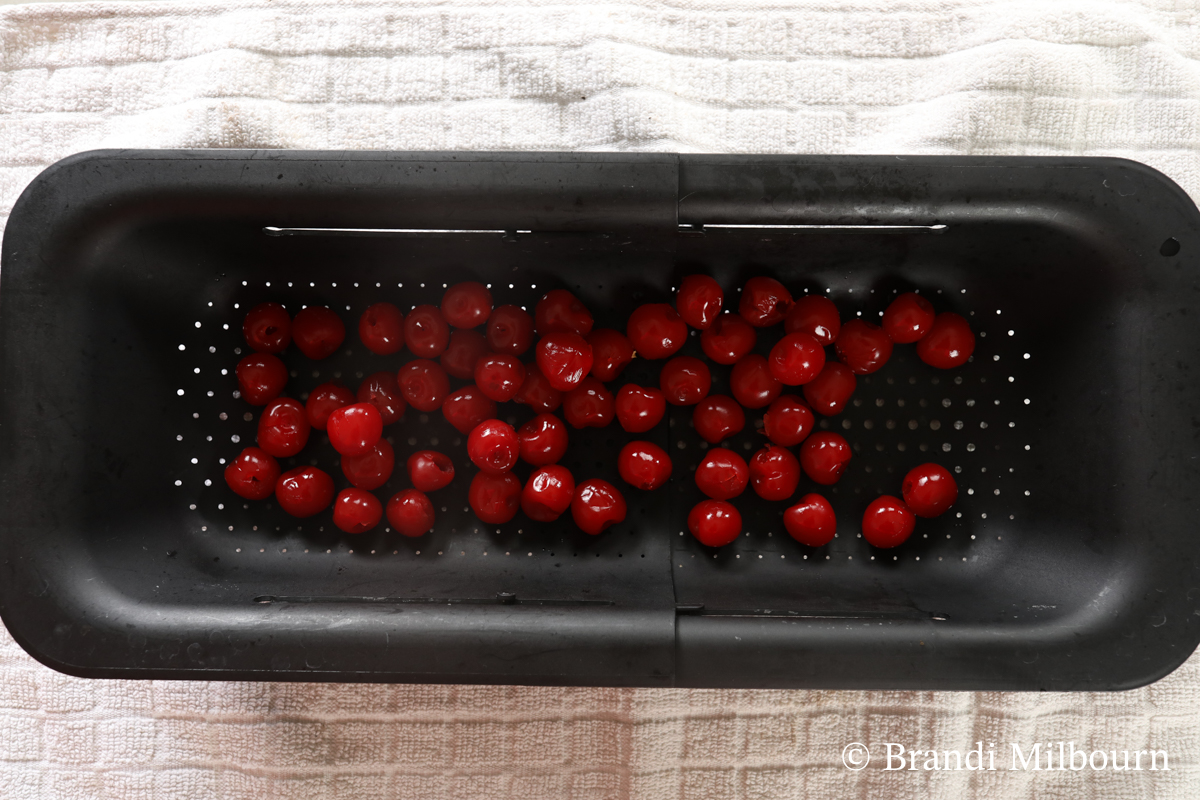 Place cherries in a strainer in the sink then  remove stems. 