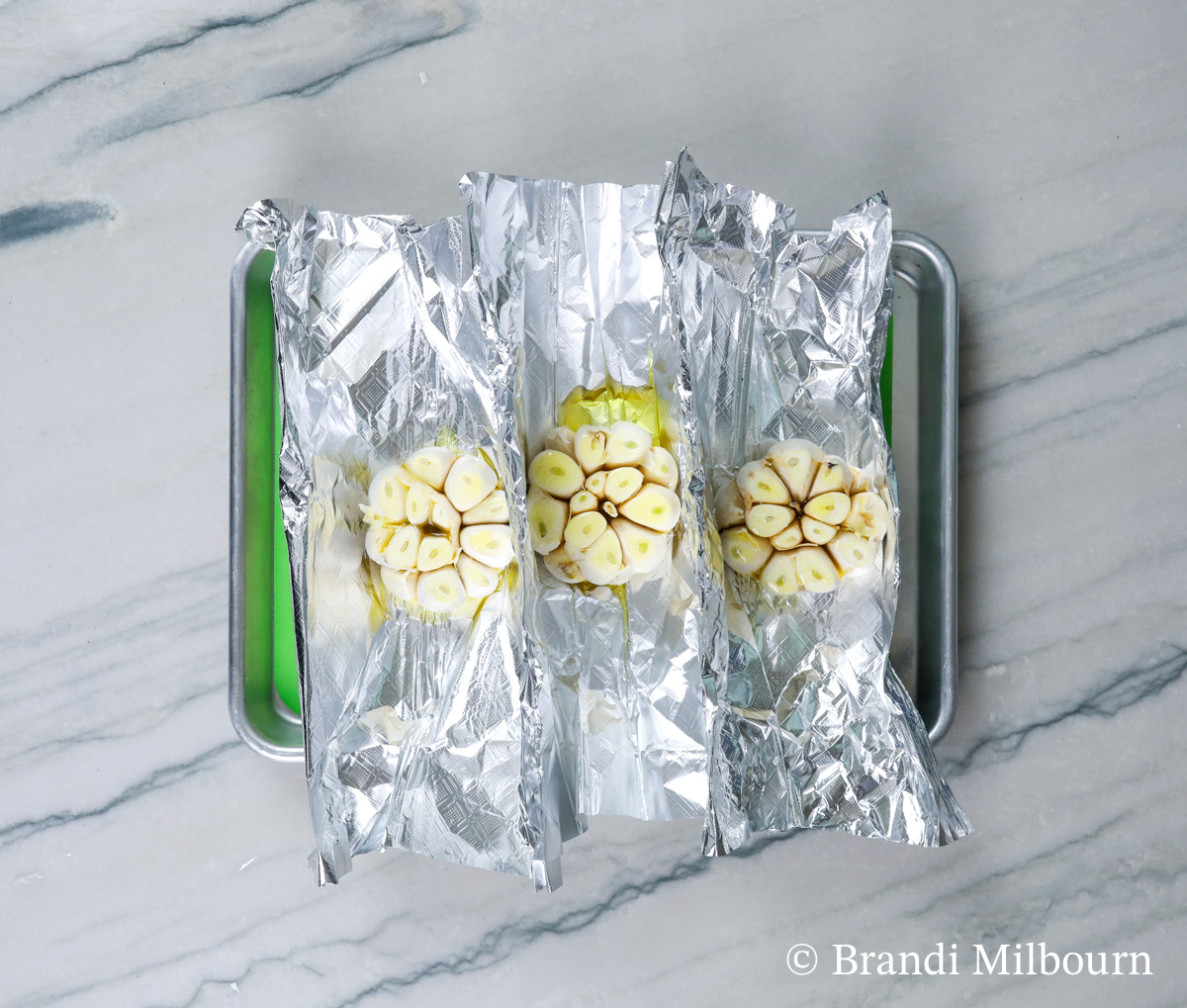 cut and peeled garlic heads on foil with olive oil poured over tip on baking sheet