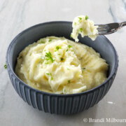 Bowl of the best mashed potatoes, with fork full of potatoes above bowl