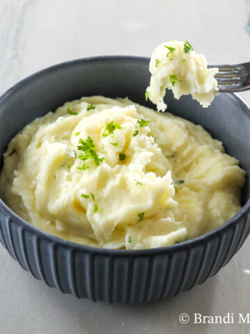 Bowl of the best mashed potatoes, with fork full of potatoes above bowl