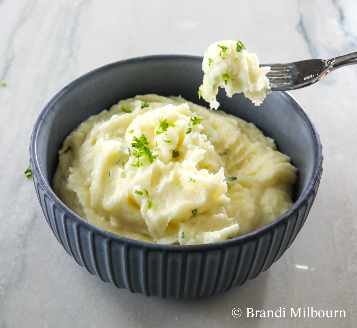 Bowl of the best mashed potatoes, with fork full of potatoes above bowl