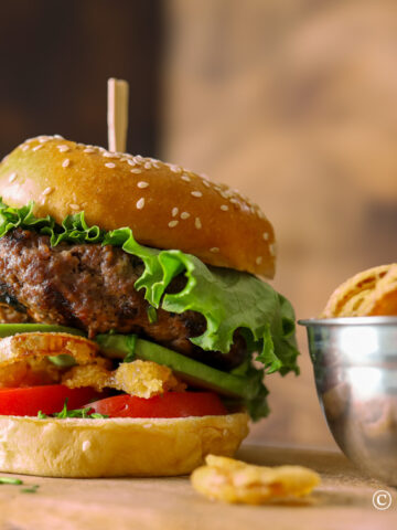 Huge burger with lettuce, deep fried onions, avocado, and tomato