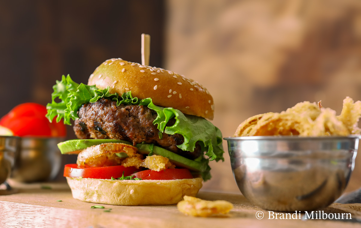 Loaded burger with tomatoes, fried onions, avocado, and lettuce.