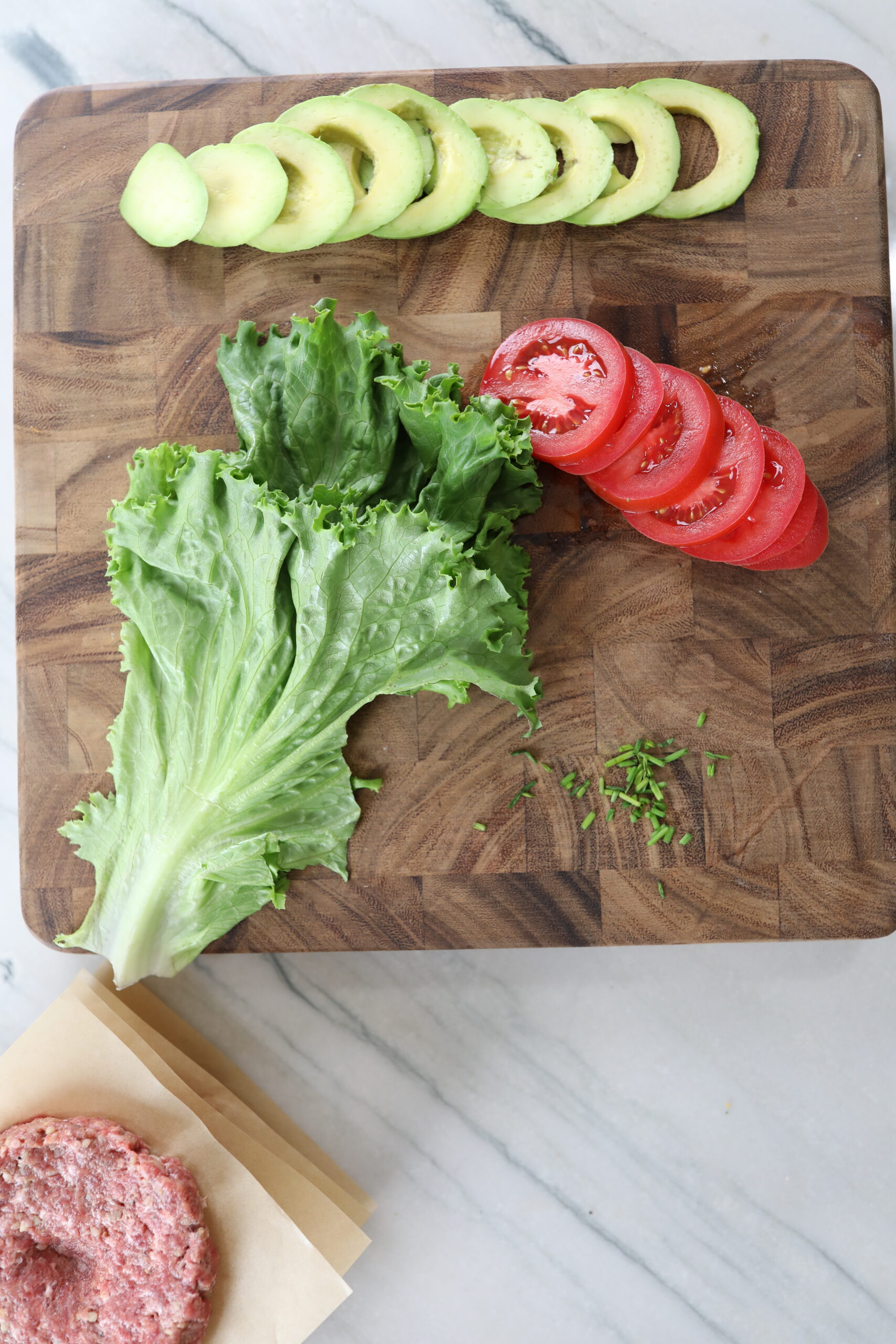 sliced tomatoes, sliced avocado, lettuce and burger patties. 